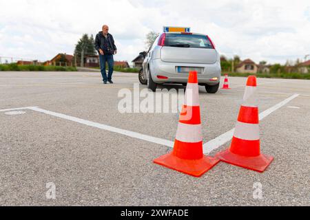 Das Mädchen übt das Parken auf dem Polygon, während ihr Lehrer sie von draußen beobachtet. Stockfoto