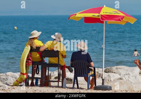 RNLI Rettungsschwimmer sitzen unter einem Regenschirm im Dienst in Avon Beach, Christchurch, Großbritannien Stockfoto