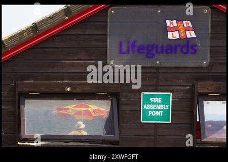 Blick durch das Fenster Einer hölzernen Rettungshütte eines RNLI Rettungsschwimmers auf Duty Under an Umbrella, Avon Beach, Christchurch, Großbritannien Stockfoto