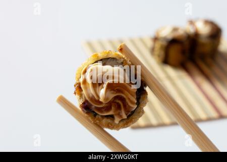 Zwei Essstäbchen mit einem heißen Brötchen, das mit Frischkäse und Tara-Sauce bedeckt ist. Stockfoto