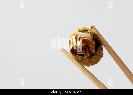 Zwei Essstäbchen mit einem heißen Brötchen, das mit Frischkäse und Tara-Sauce auf weißem Hintergrund bedeckt ist. Stockfoto