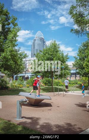 Cincinnati, Ohio, 30. Juli 2022: Kinder spielen auf dem Spielplatz im Smale Riverfront Park mit dem Great American Tower im Hintergrund Stockfoto