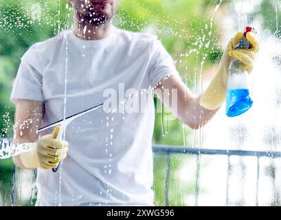 Ein Mann in einem weißen Hemd und gelben Schutzhandschuhen reinigt ein Fenster Stockfoto