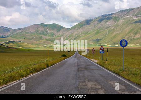 Die gerade Straße auf dem Plateau Castelluccio di Norcia in Umbrien, Italien, an einem sonnigen und bewölkten Sommertag Stockfoto