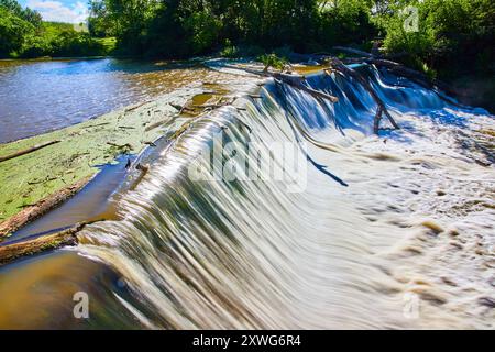 Wasserfall über Damm im üppigen Wald mit sonnendurchfluteten Sparkles Stockfoto