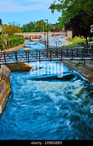 Fließender Kanal mit Fußgängerbrücke in der Tagesperspektive von Urban Park Stockfoto