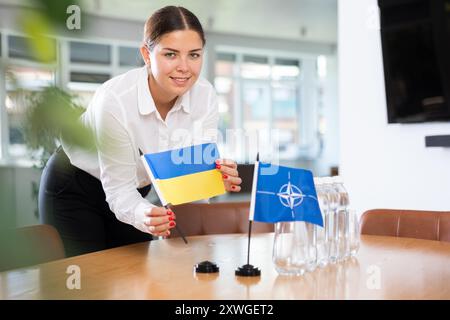 Geschäftsfrau, die die Flaggen der NATO und der Ukraine für Präsentationen und Verhandlungen arrangiert Stockfoto