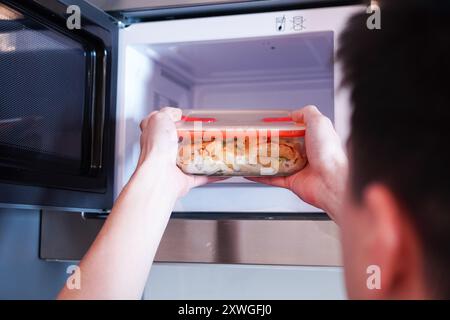 Junger Mann erwärmt hitzebeständiges Glas Tupperware in der Mikrowelle in seinem Büro Stockfoto