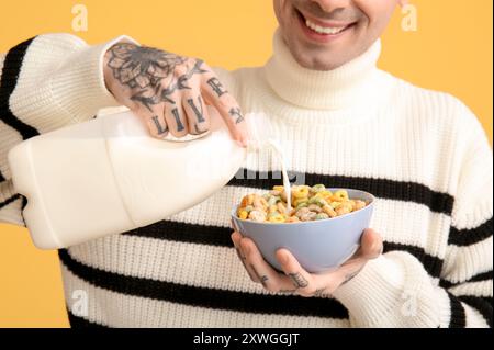 Mann, der Milch in eine Schüssel mit Müsliringen auf gelbem Hintergrund gießt Stockfoto