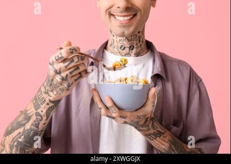 Mann hält Schüssel mit Müsliringen und Löffel auf rosa Hintergrund Stockfoto