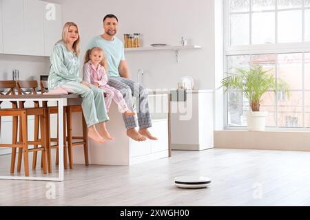 Glückliche Familie mit Roboter-Staubsauger auf dem Boden in der Küche Stockfoto