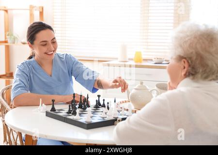 Physiotherapeutin mit einer älteren Frau, die Schach am Tisch in der Küche spielt Stockfoto