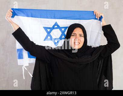 Eine aufgebrachte muslimische Frau im traditionellen schwarzen Hidschab hält die Flagge Israels Stockfoto