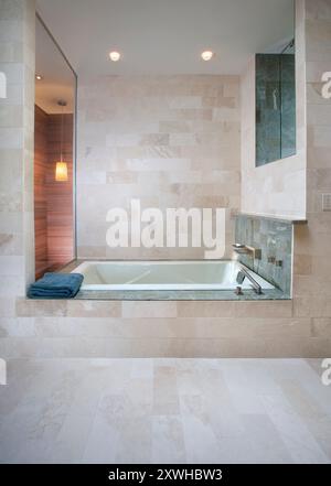Moderne Badewanne mit cremefarbenen Steinfliesen und zwei Fenstern Stockfoto