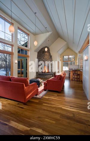 Lange offene Etage der modernen Hütte mit Steinkamin und großen Fenstern zeigen den Winter draußen Stockfoto