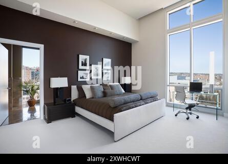 Modernes braunes und weißes Schlafzimmer mit großem Fenster und Tür zum Badezimmer Stockfoto