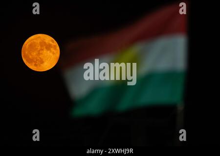 Duhok, Irak. August 2024. Der Supermond erhebt sich hinter der Flagge der Region Kurdistan am Himmel der nordirakischen Stadt Duhok. Quelle: SOPA Images Limited/Alamy Live News Stockfoto