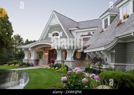 Nähere Sicht auf ein großes Haus im Landhausstil mit grünem Gras und Blumen in der Abenddämmerung Stockfoto