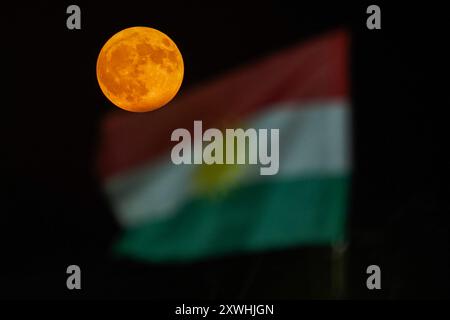 Duhok, Irak. August 2024. Der Supermond erhebt sich hinter der Flagge der Region Kurdistan am Himmel der nordirakischen Stadt Duhok. (Foto: Ismael Adnan/SOPA Images/SIPA USA) Credit: SIPA USA/Alamy Live News Stockfoto