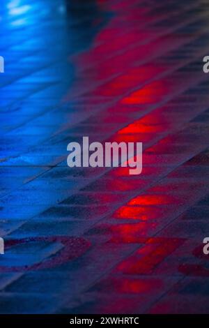 Rote und blaue Reflexe von Neonlichtern auf nassem Asphalt in einer großen Metropole. Nachtlichter der Stadt. Straßenbeleuchtung bei Nacht. Stockfoto
