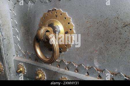 Alter Türgriff aus Eisen mit goldener Farbe an der Eisentür, alte Eisentür, silberfarbene Tür Stockfoto