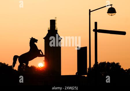 Hannover, Deutschland. August 2024. Die Silhouette des Sächsischen Pferdes vor dem Welfenschloss an der Leibniz Universität Hannover hebt sich vor dem sonnenaufgangsfarbenen Morgenhimmel ab. Quelle: Julian Stratenschulte/dpa/Alamy Live News Stockfoto