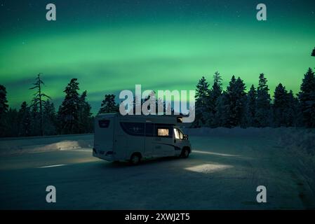 Nordlichter über einem Wohnmobil und einem schneebedeckten Wald bei Nacht (Lappland, Finnland) ESP: Aurora boreal, erfahre una autocaravana y un bosque nevado, Laponia Stockfoto