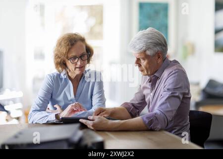 Symbolfoto. Eine Frau und ein Mann sitzt zusammen an einem Tisch mit einem Tablet und unterhält sich. Berlin, 13.08.2024. Berlin Deutschland *** Sy Stockfoto