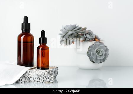 Tropfflaschen aus Braunglas auf Steinplattform mit Sukkulenten Stockfoto