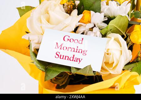 GUTEN MORGEN WELT auf einer weißen Visitenkarte vor einem Hintergrund von frischen Blumen. Das Konzept von Liebe und Freude Stockfoto