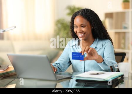 Schwarze Geschäftsfrau kauft online mit Laptop und Kreditkarte, die zu Hause arbeitet Stockfoto