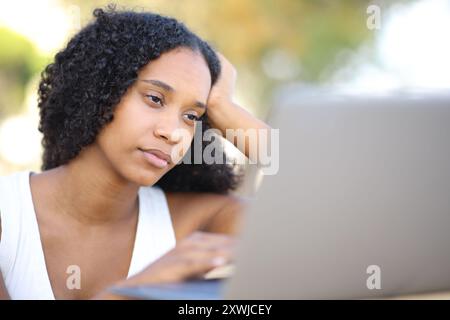 Ernsthafte schwarze Frau überprüft draußen den Laptop Stockfoto