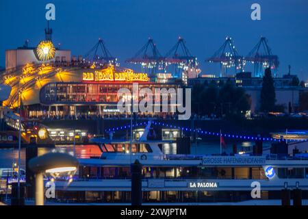 HAMBURG, DEUTSCHLAND - 15. AUGUST 2024: Abend im Hamburger Hafen. Im Vordergrund sind beleuchtete Schiffe, im Hintergrund Theater, in denen die m Stockfoto