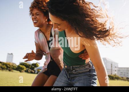 Zwei junge Freunde in ihren Zwanzigern teilen unbeschwertes Lachen und Freude, während sie gemeinsam in einem offenen grünen Park unter der Sonne spielen. Stockfoto