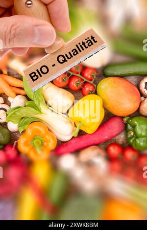 Bio-Qualität von Lebensmitteln ein Holzstempel ist beschriftet mit dem Aufdruck: Bio-Qualität über frisches Obst und Gemüse - FOTOMONTAGE *** Bio q Stockfoto