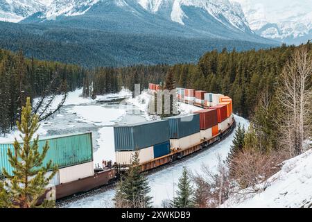 Ein Güterzug mit Containern, der im Winter durch das Bow Valley und die felsigen Berge in Morants Curve, Kanada, fährt Stockfoto