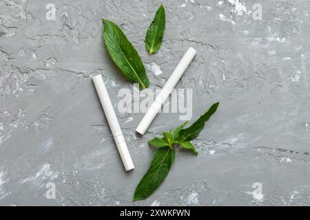 Menthol-Zigaretten und frische Minzblätter auf farbigem Hintergrund, viele Zigaretten gestapelt Draufsicht flach liegend. Stockfoto