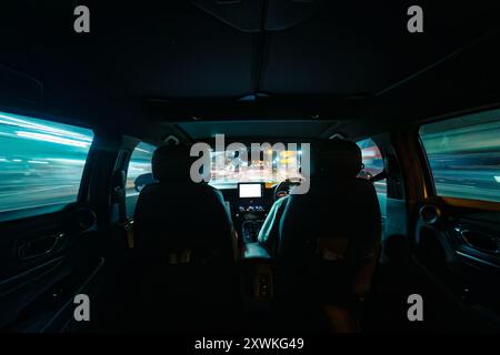 Mit dem Auto fahren Sie durch die Straße der Nachtstadt. Blick von der Rückbank und dem Armaturenbrett des Fahrzeugs Stockfoto
