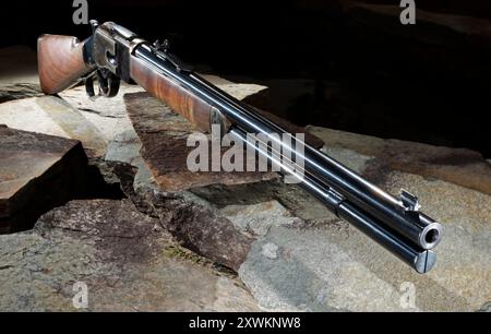 Altes Westernschiebergewehr mit gebläutem Stahl und Holzschaft draußen in der Nacht, auf mehreren großen Felsen ruht. Stockfoto