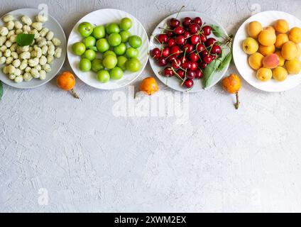 Sommerfrüchte-Konzept, grüne Pflaumen, Mickel, Aprikosen, rote Kirschen auf Teller Stockfoto