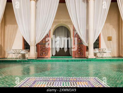 Eleganter Innenhof im Le Jardin Secret in Marrakesch mit grünen Mosaikfliesen, weißen Vorhängen, luxuriösem marokkanischem Design und traditioneller Architektur Stockfoto