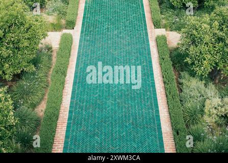 Blick aus der Vogelperspektive auf einen kunstvollen, grün gekachelten Gartenweg aus türkisfarbenen marokkanischen Fliesen, mit üppigem Grün im formellen botanischen Garten, Marrakesch, Marokko Stockfoto