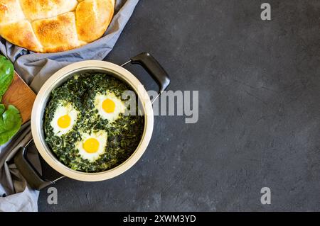 Gebratener Spinat und Spiegeleier im Stewpot mit frischem Spinatgemüse auf rustikalem Tisch Stockfoto