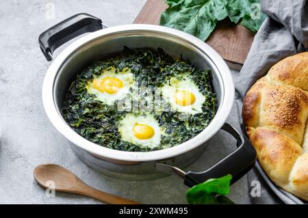 Gebratener Spinat und Spiegeleier im Stewpot mit frischem Spinatgemüse auf rustikalem Tisch Stockfoto