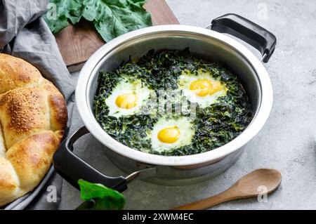 Gebratener Spinat und Spiegeleier im Stewpot mit frischem Spinatgemüse auf rustikalem Tisch Stockfoto
