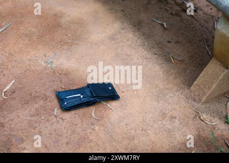 Eine Ledergeldbörse liegt verlassen auf einem unbefestigten Weg und deutet auf einen vergesslichen Moment oder ein potenzielles Rätsel hin. Stockfoto