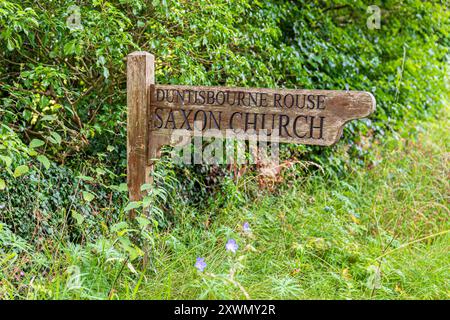 Das hölzerne Schild zeigt auf die sächsische Kirche im Dorf Duntisbourne Rouse in Cotswold, Gloucestershire, England Stockfoto