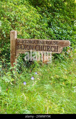 Das hölzerne Schild zeigt auf die sächsische Kirche im Dorf Duntisbourne Rouse in Cotswold, Gloucestershire, England Stockfoto