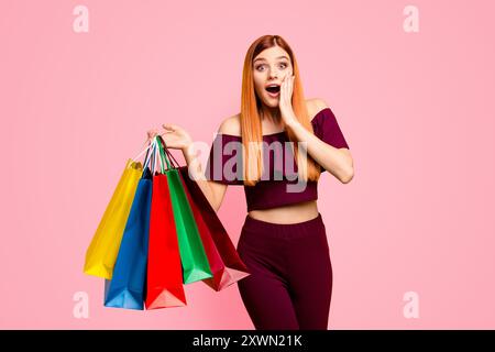 Der Black friday wunderte sich über eine junge Frau mit überraschtem Gesicht, die seine Hand nahe der Wange hält, mit weit offenen Augen und Mund in der anderen Hand, die Einkäufe hält Stockfoto