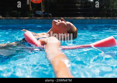 Eine ältere Frau schwimmt ruhig in einem Swimmingpool mit geschlossenen Augen und genießt die Entspannung des Wassers an einem hellen sonnigen Tag Stockfoto